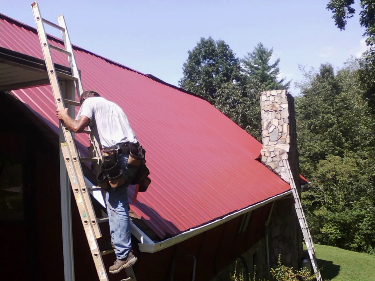 Roofer on a ladder beside a red metal roof and stone chimney in Oak Lawn