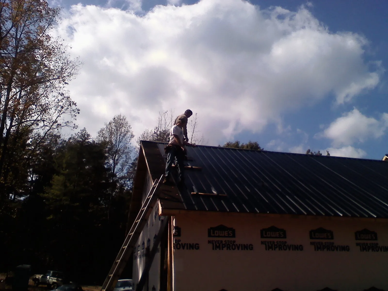 Roofer fastening dark metal panels high against a cloudy sky, from a Roof Inspection job in Oak Lawn