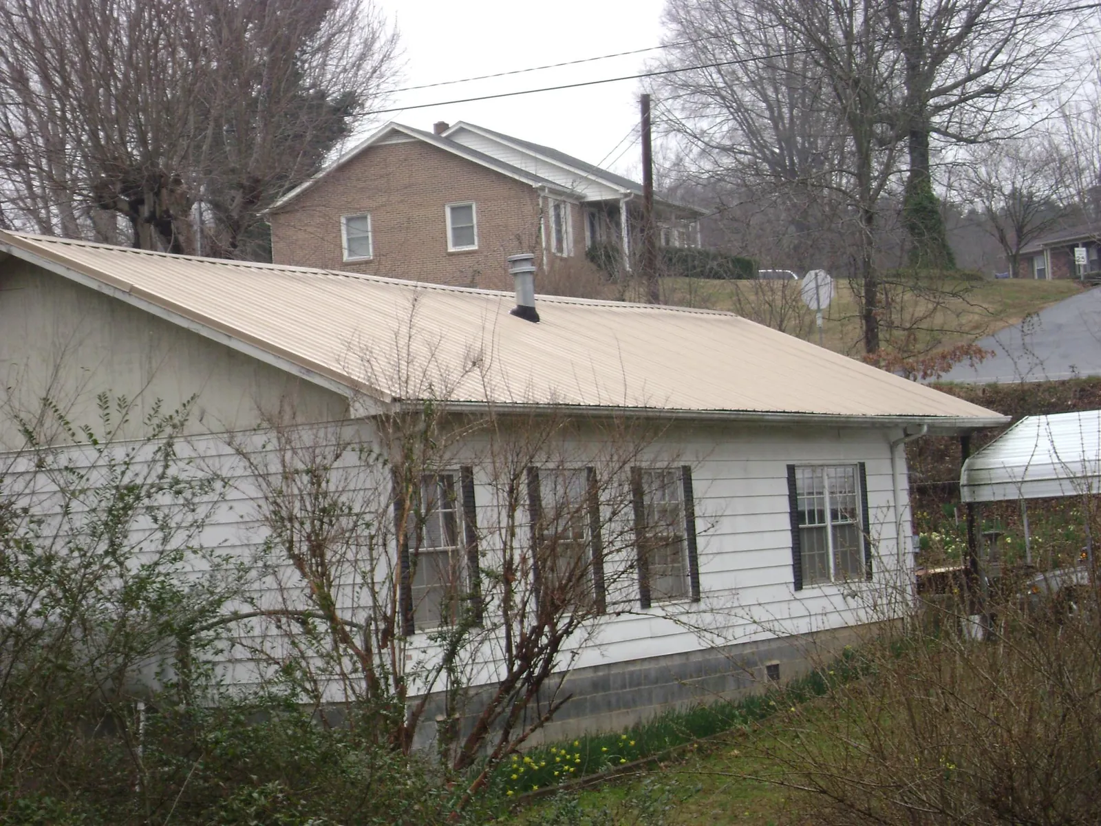 Tan metal roof on a white sided house set into a hillside — Commercial Roofing by Roofing Brothers in Oak Lawn